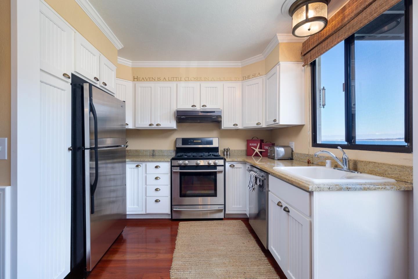 Kitchen with white cabinets, stainless steel appliances, and a farmhouse sink beside a water-view window.