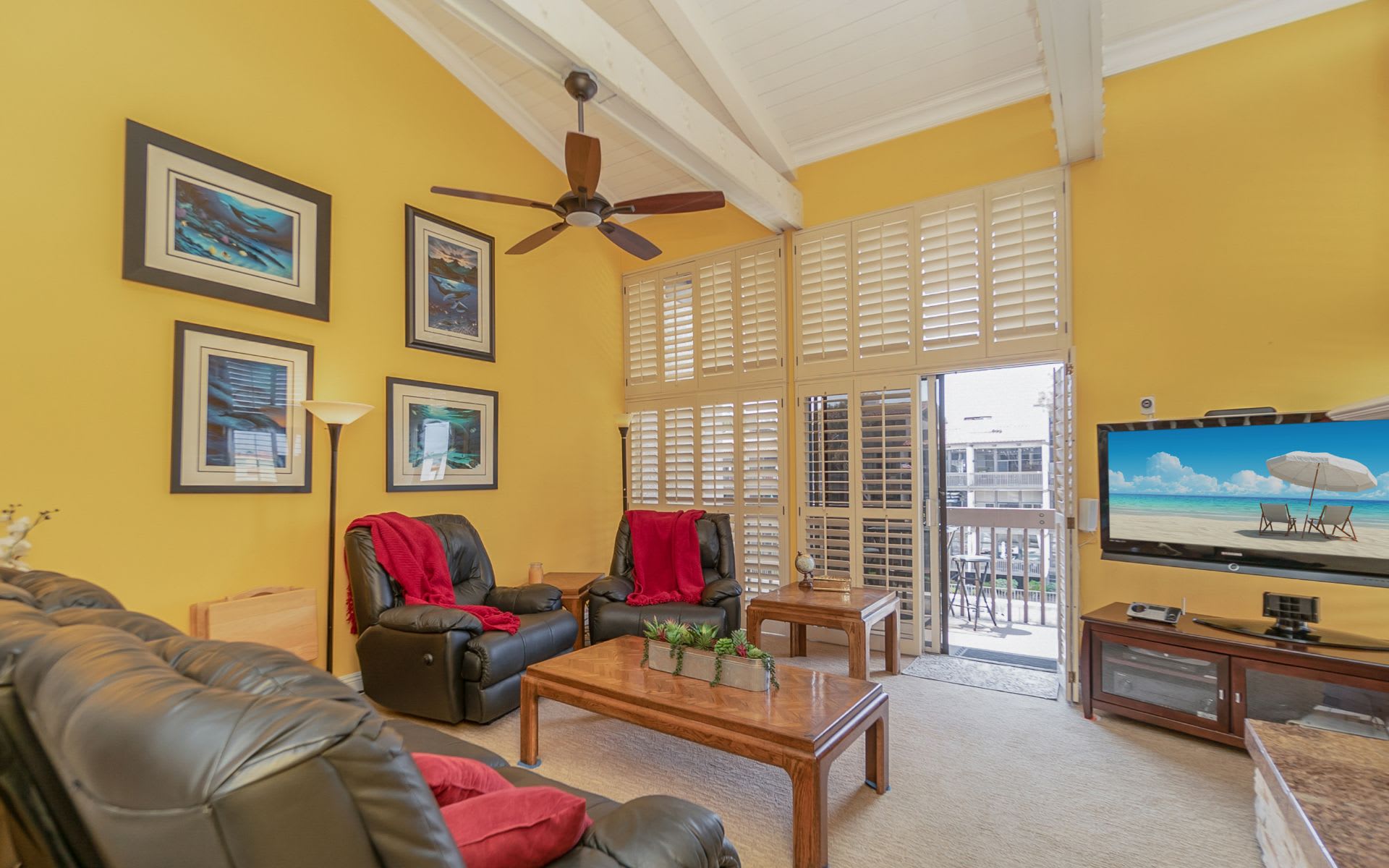 Living room with yellow walls, vaulted ceiling, leather recliners, and plantation-shuttered balcony doors.