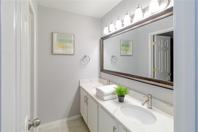 Bathroom vanity with a large framed mirror, bright lights, folded towels, and a potted plant.