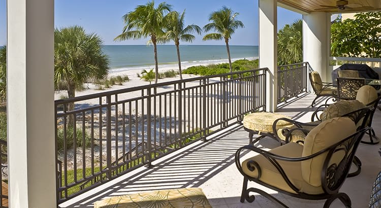 A beautiful outdoor patio or balcony overlooking a beach. The space is furnished with comfortable chairs and seating, offering a relaxing spot to enjoy the view.