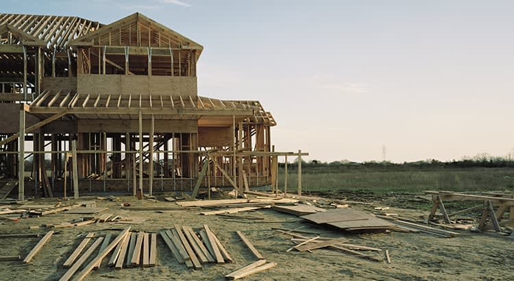 This image depicts a large, elevated home being built near a waterfront, with construction materials scattered around. It could represent real estate development or home building in coastal or flood-prone areas.