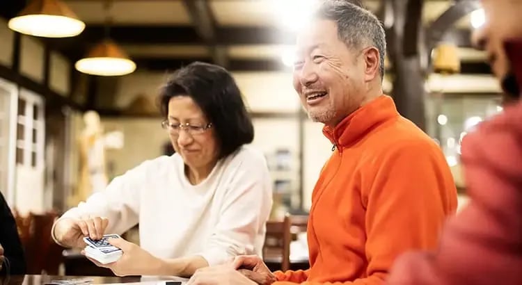 An older couple sitting at a table in a warm, well-lit environment, smiling and enjoying each other’s company.