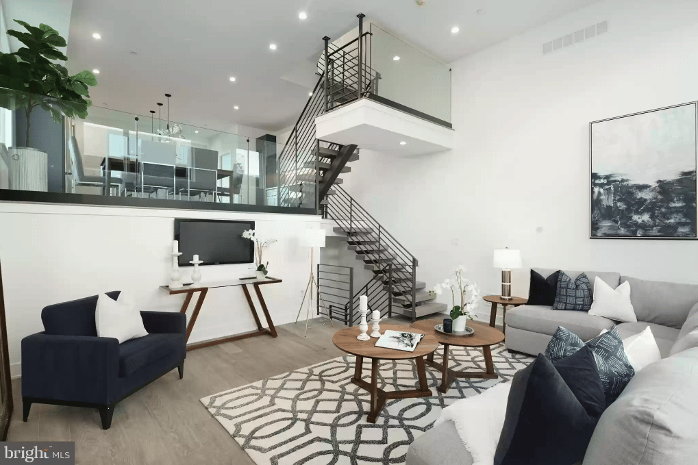 Modern living room with a double-height ceiling, mezzanine, and black metal staircase.