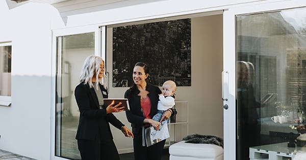 A woman holding a clipboard, standing with another woman holding a baby, possibly discussing something.