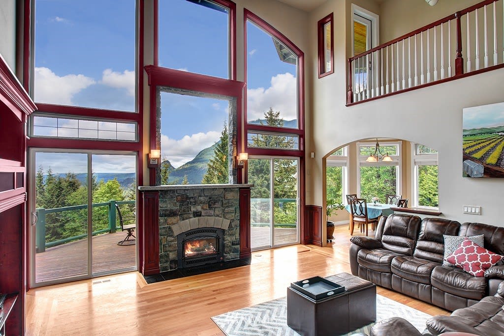 Living room with a tall stone fireplace, soaring windows, and mountain views.