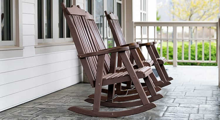 A porch with wooden rocking chairs. The porch has white railings and overlooks a yard.