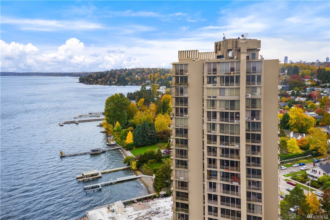 Luxury high-rise condo tower overlooking a serene lakeside with autumnal trees.