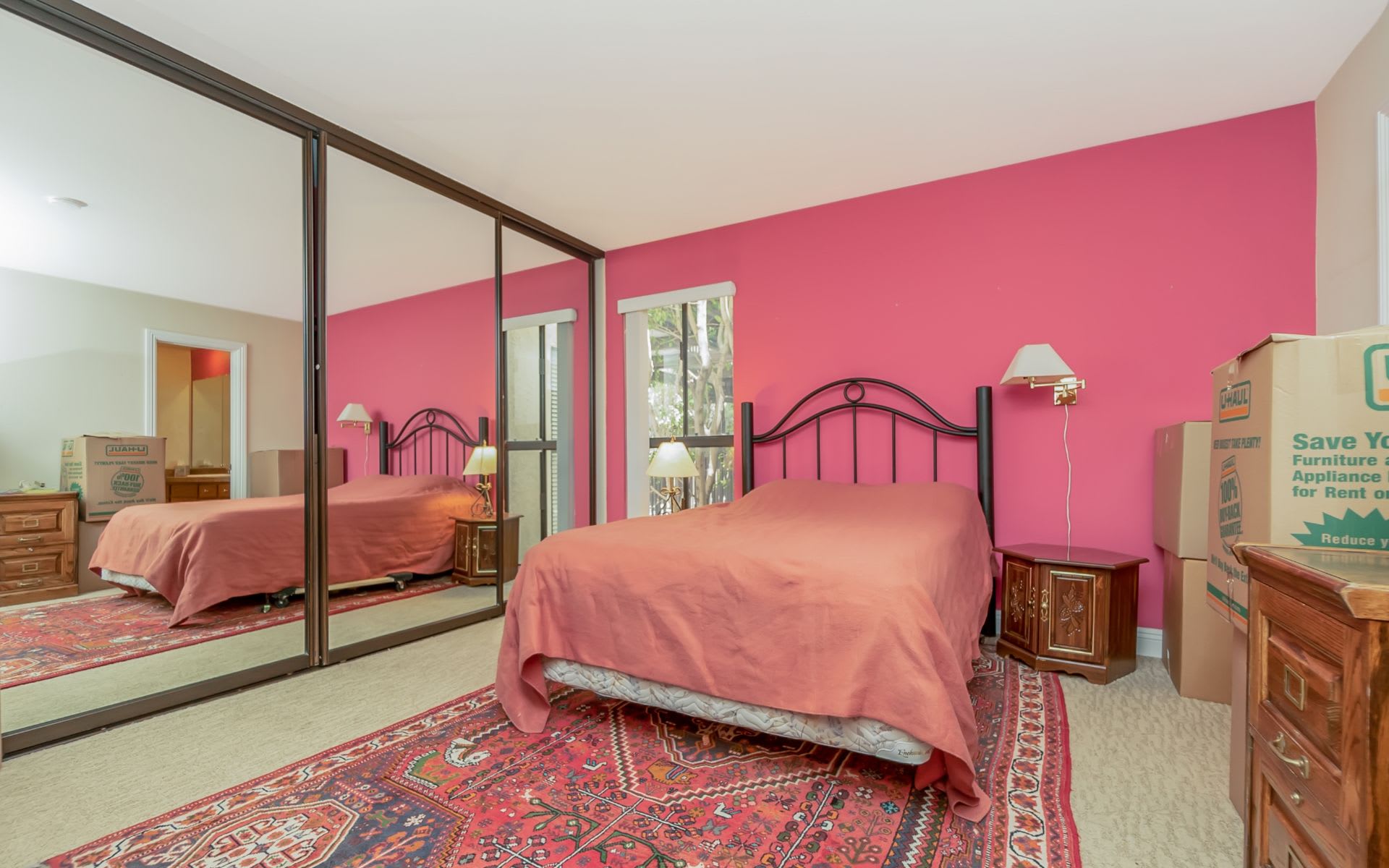 Bedroom with a pink accent wall, mirrored closet doors, and a bed over patterned rugs.