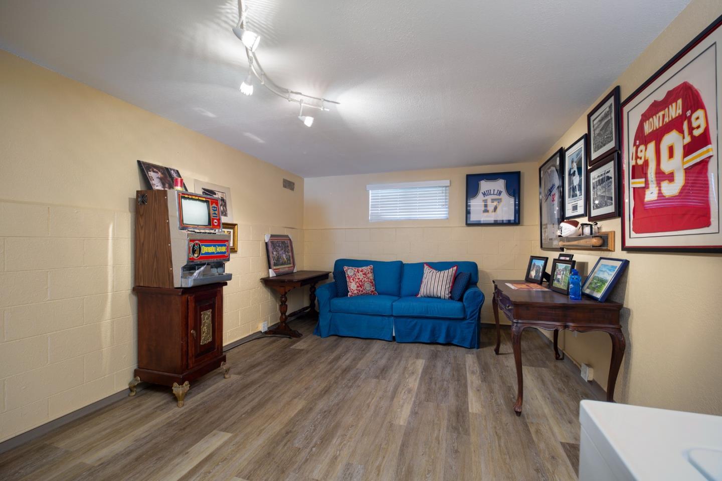 Furnished recreation room with a blue sofa, vintage arcade machine, and framed sports jerseys.