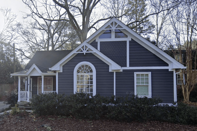 An exterior view of a house with a large front yard and trees, featuring a classic architectural style.