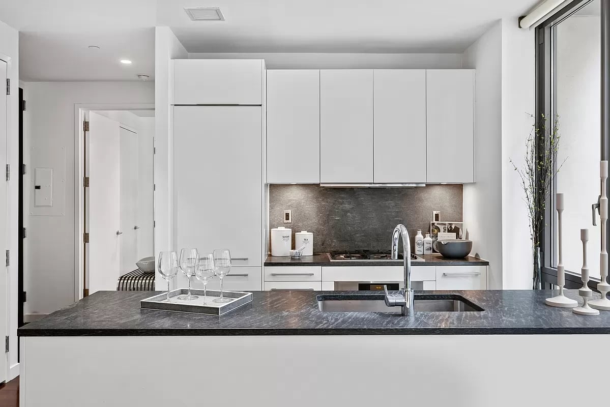 Modern kitchen with white cabinetry, a dark stone island, and tall windows.