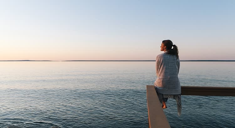 A serene setting with a person sitting near a body of water, perhaps symbolizing tranquility or life decisions.