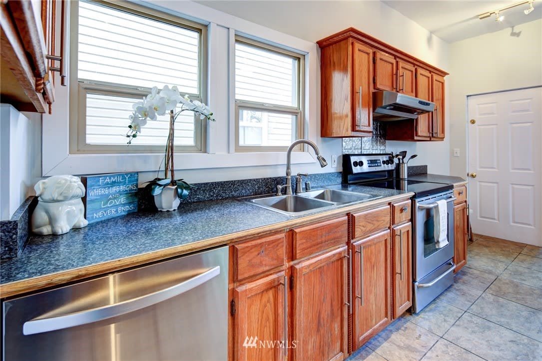 Kitchen with reddish wood cabinets, dark countertops, stainless steel appliances, and two windows above the sink.