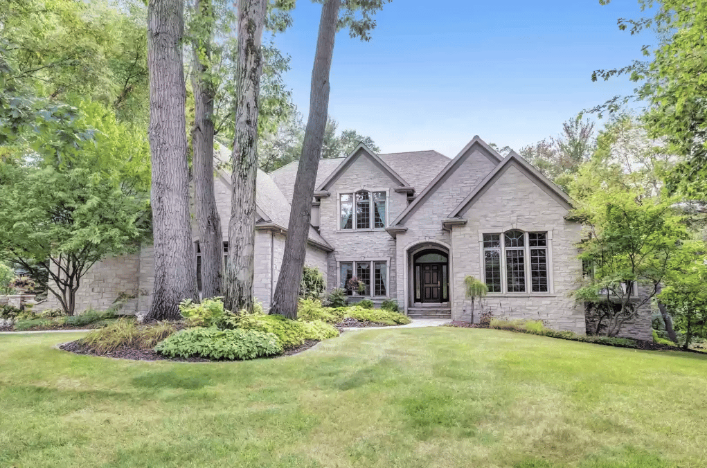 Two-story stone house with steep gables, mature trees, and a broad front lawn.