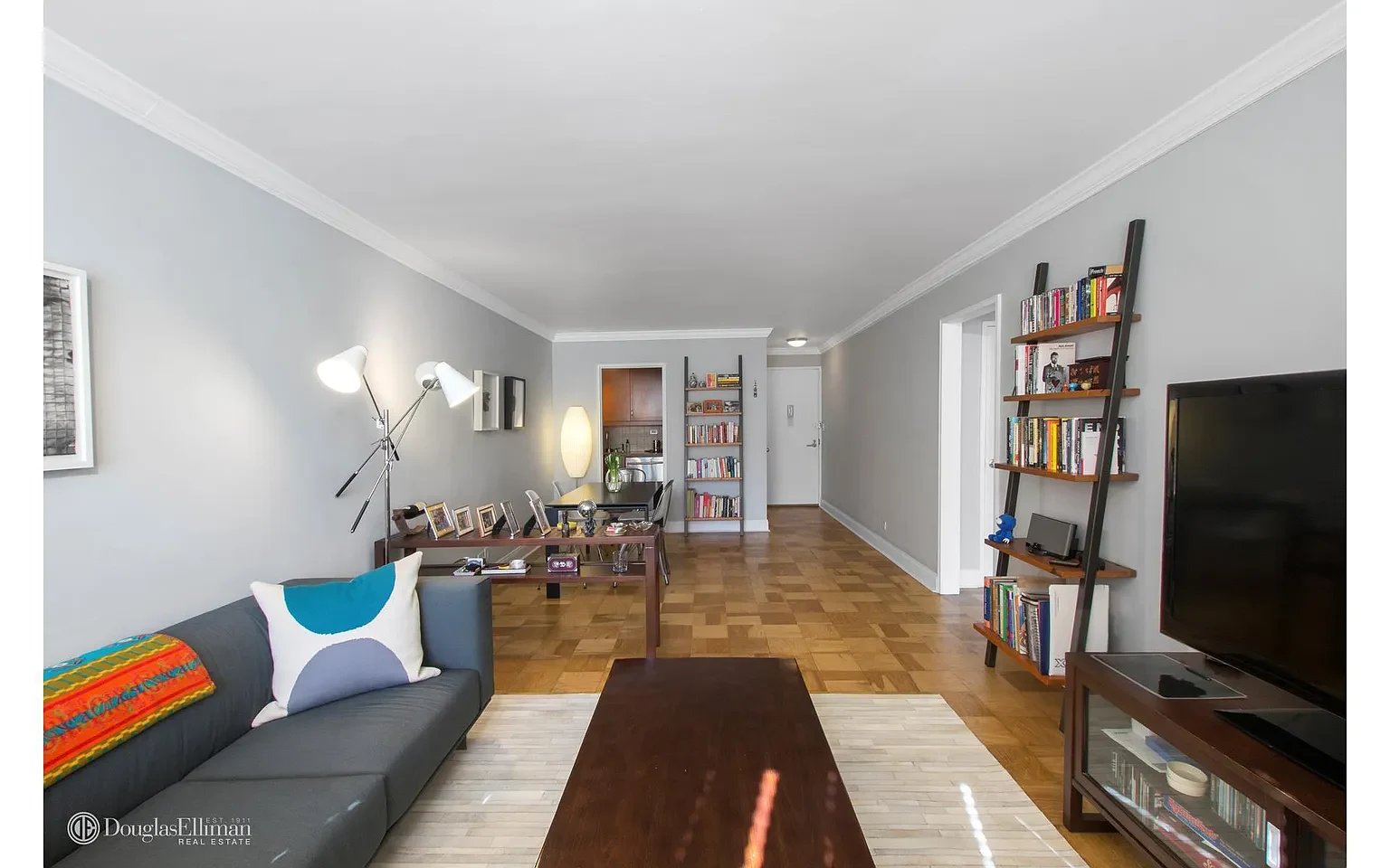 Furnished apartment living room with a gray sofa, parquet floors, and ladder-style bookshelves.