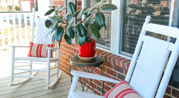 White rocking chairs and a red-potted plant on a brick-lined porch.