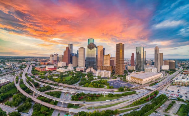 Downtown Houston skyline and freeway interchanges beneath a vivid sunset sky.