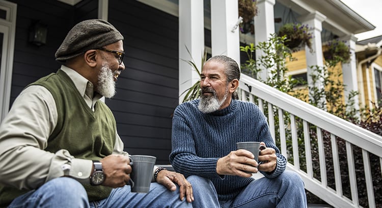 two older men having a conversation on a porch.