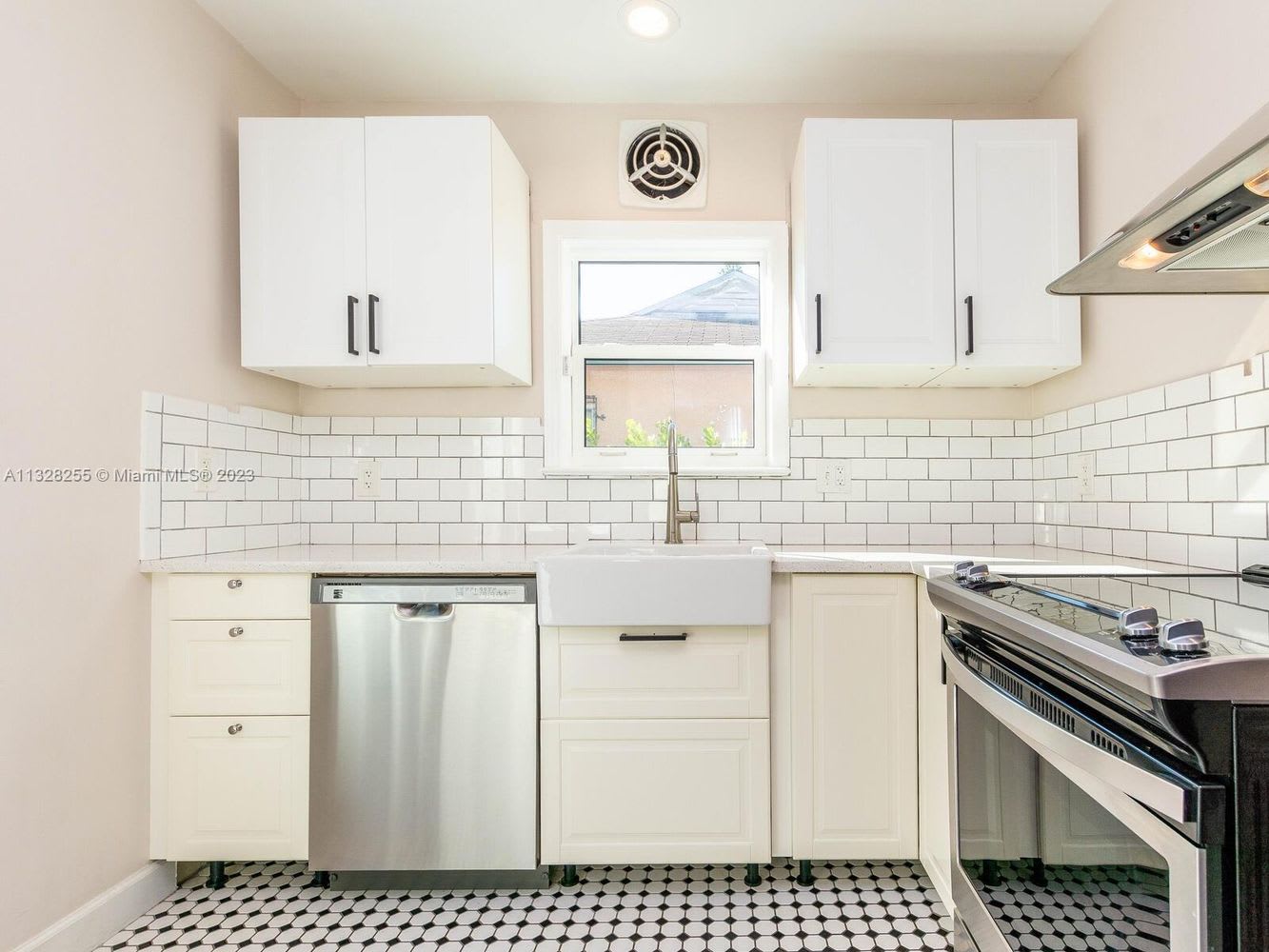 Bright kitchen with white cabinets, stainless steel appliances, farmhouse sink, and black-and-white hexagonal tile floor.