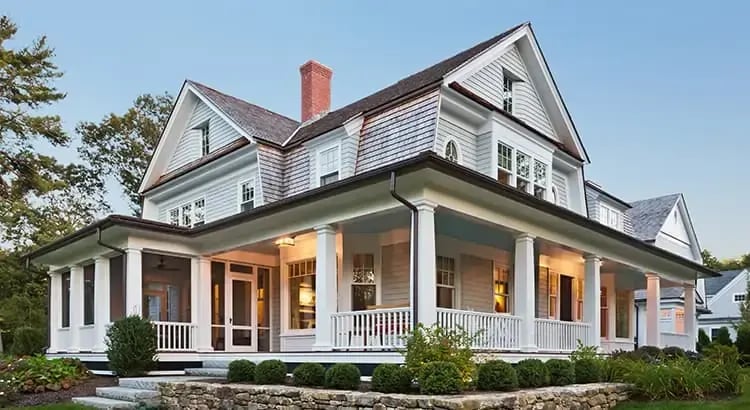 A large, elegant house with a wrap-around porch and classic architectural details. The house is surrounded by a well-kept lawn and trees.