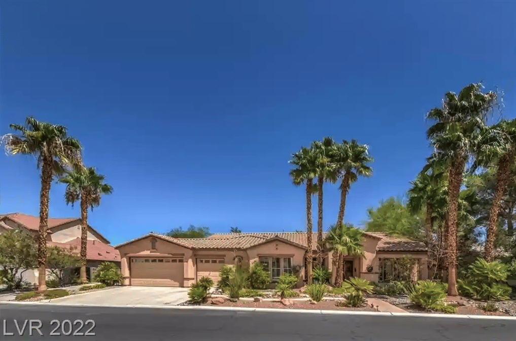 Single-story stucco home with a two-car garage, desert landscaping, and tall palm trees.