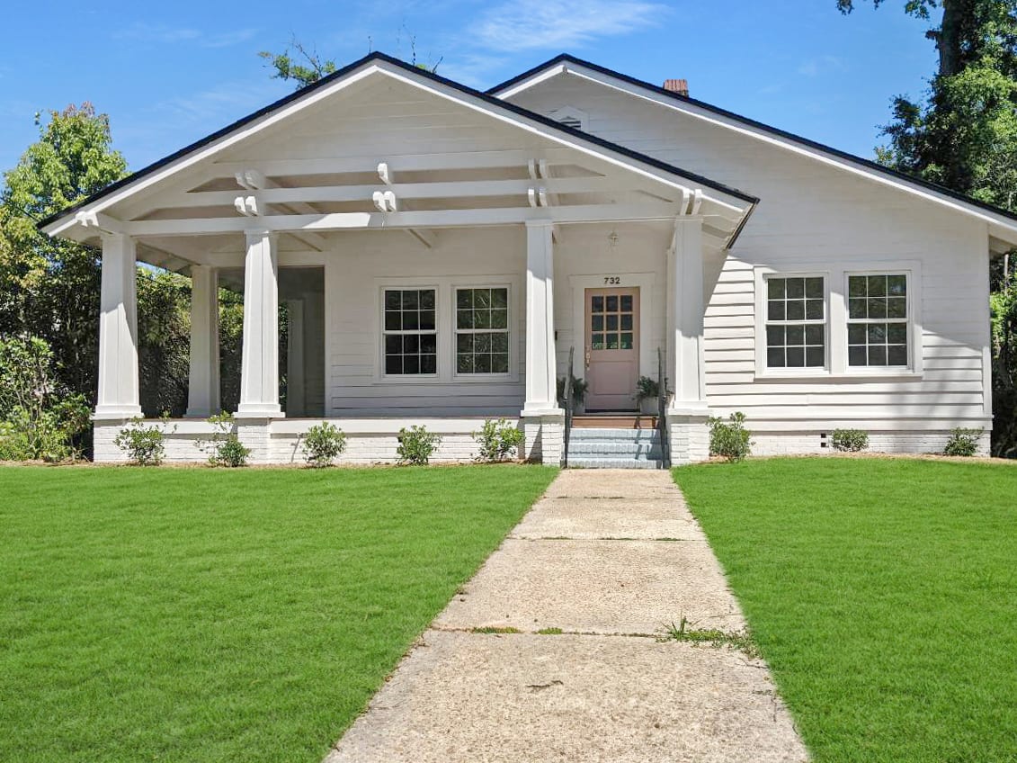 A front view of a white single-story house with a manicured lawn and a pathway leading to the porch.