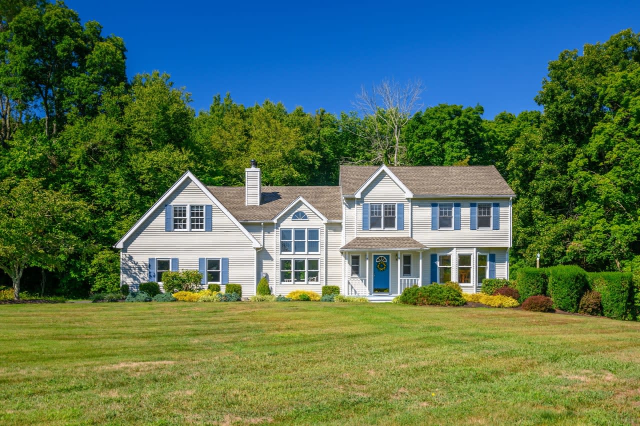 A white colonial house with a lush green lawn in front of it in Newtown, Connecticut.