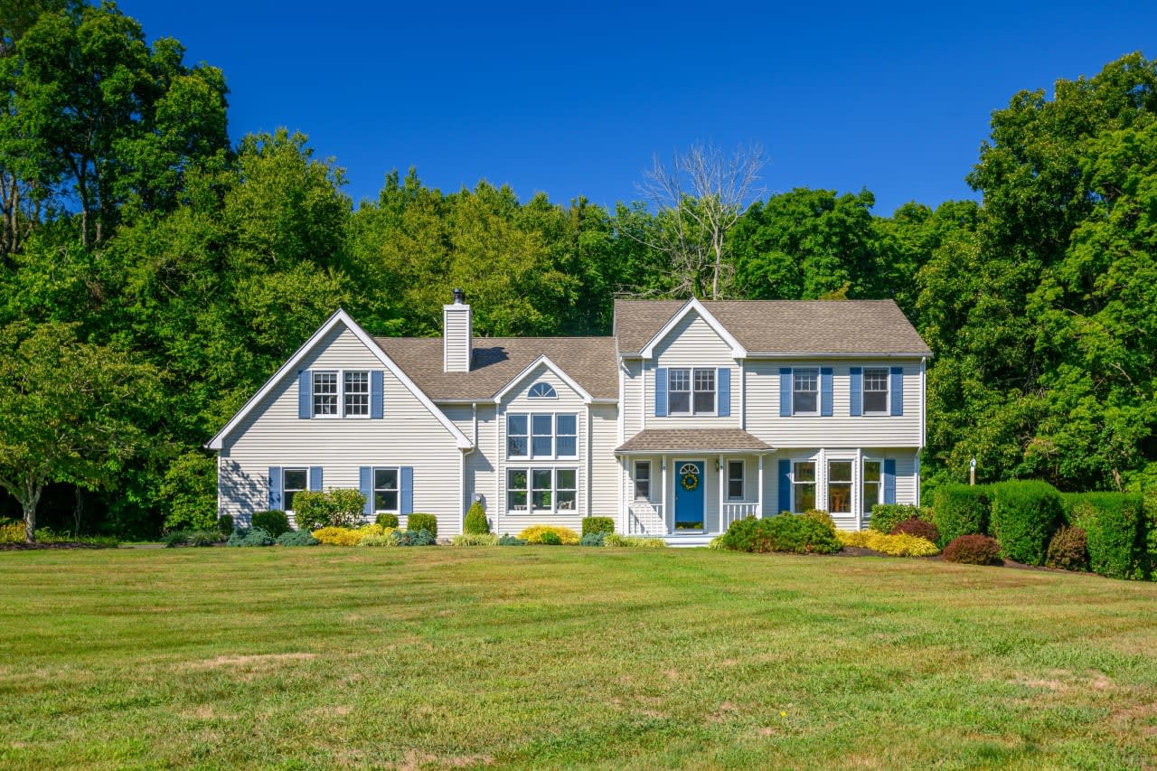 A white colonial house with a lush green lawn in front of it in Newtown, Connecticut.