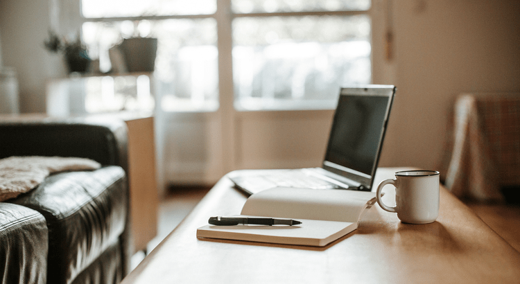 A photo of a home office setup with a laptop, coffee mug, and notebook on a desk.