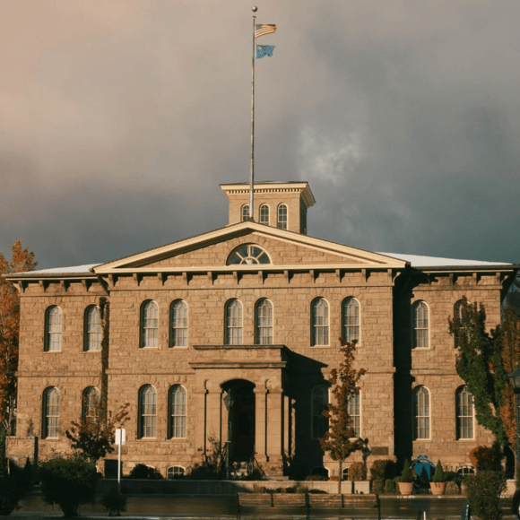 Stone civic building with arched windows and American and blue flags flying above its roof.