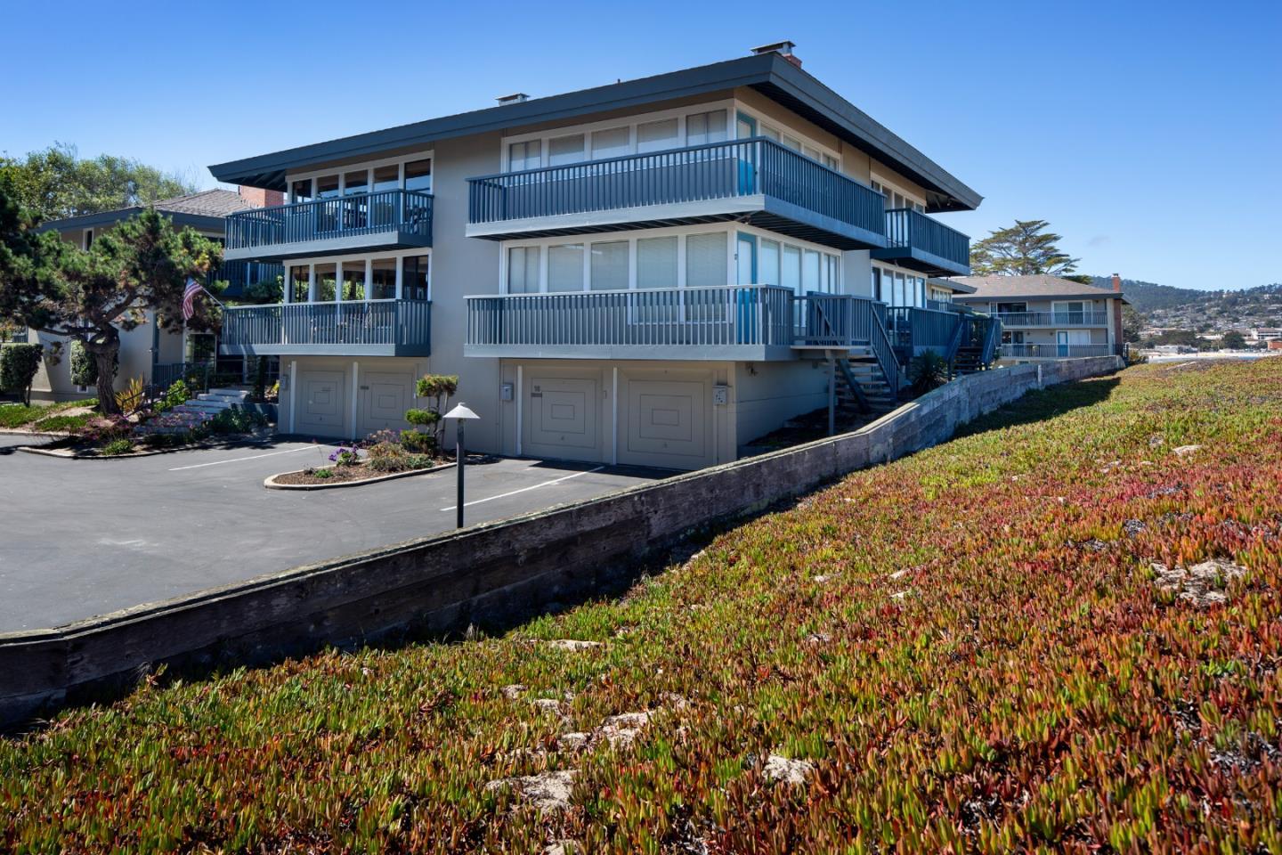 Modern home with blue-railed balconies beside a sloping bed of succulent groundcover.