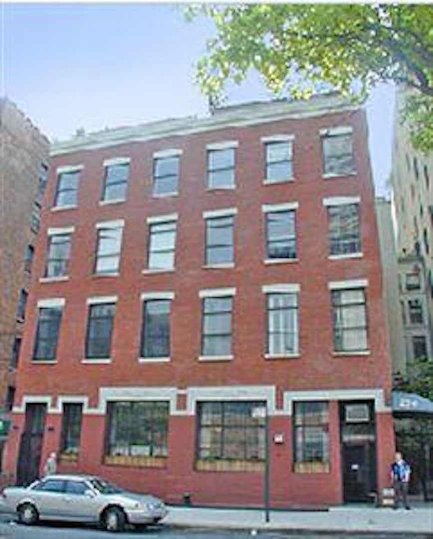 Red-brick multi-story building with rows of windows and storefront-style windows along the sidewalk.