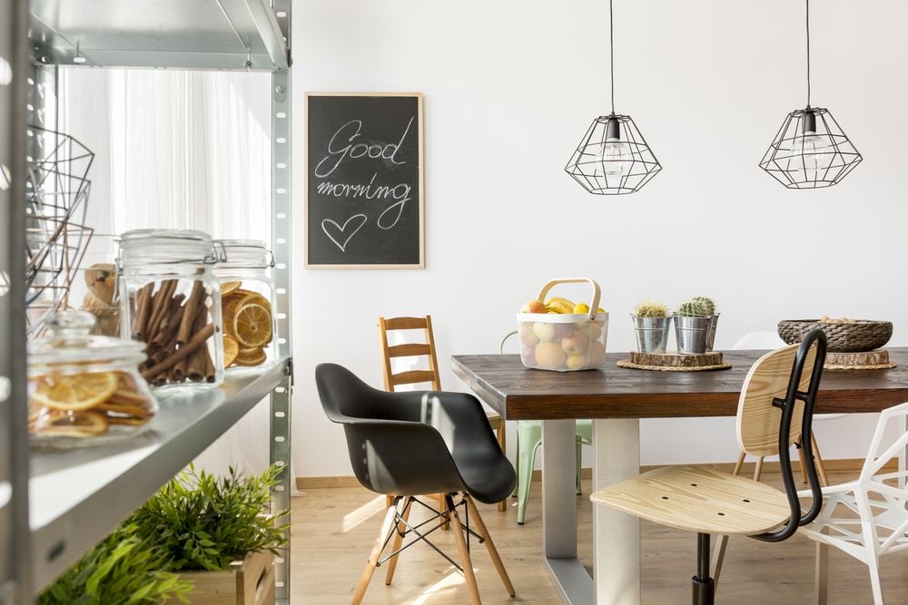 Bright dining area with a dark wood table, geometric pendant lights, and open shelving with glass jars.