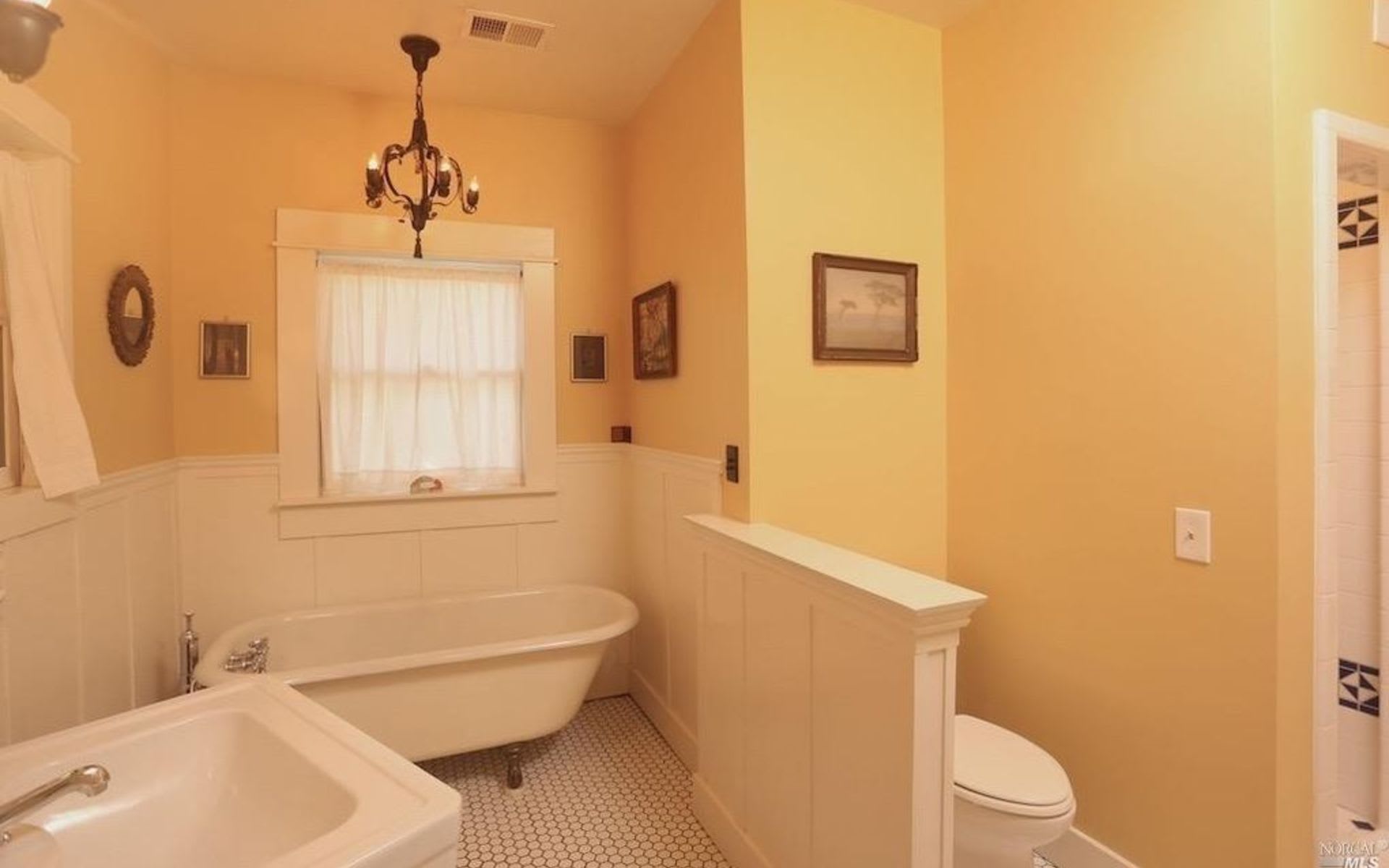 Bathroom with a clawfoot tub beneath a curtained window and a toilet behind a half wall.