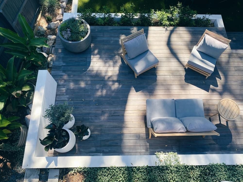 Overhead view of a furnished wood deck with cushioned seating and potted plants.
