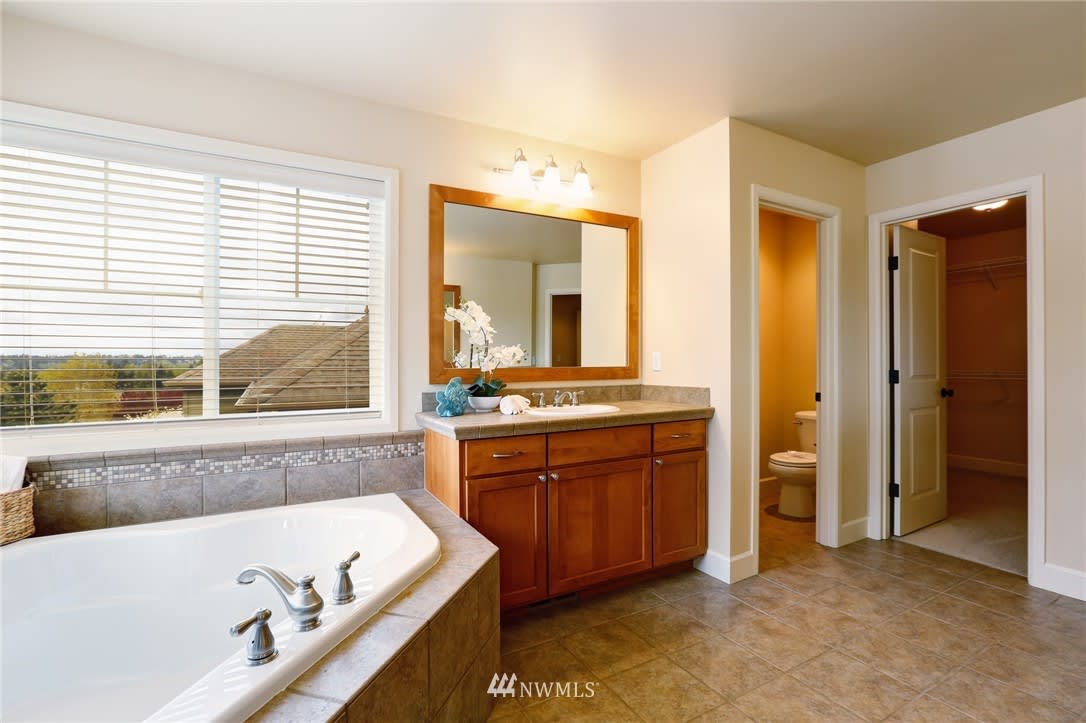 Primary bathroom with corner soaking tub, wide window, and wood vanity.