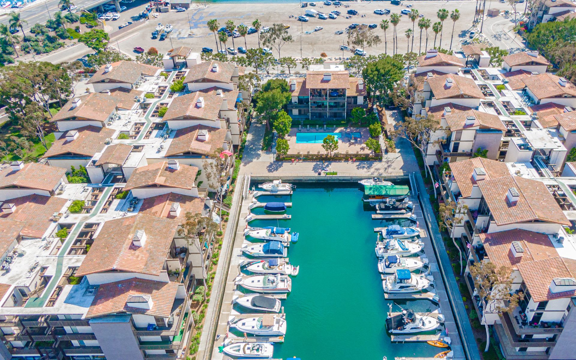 Waterfront condominiums surround a boat-filled marina channel, with a shared pool between the buildings.