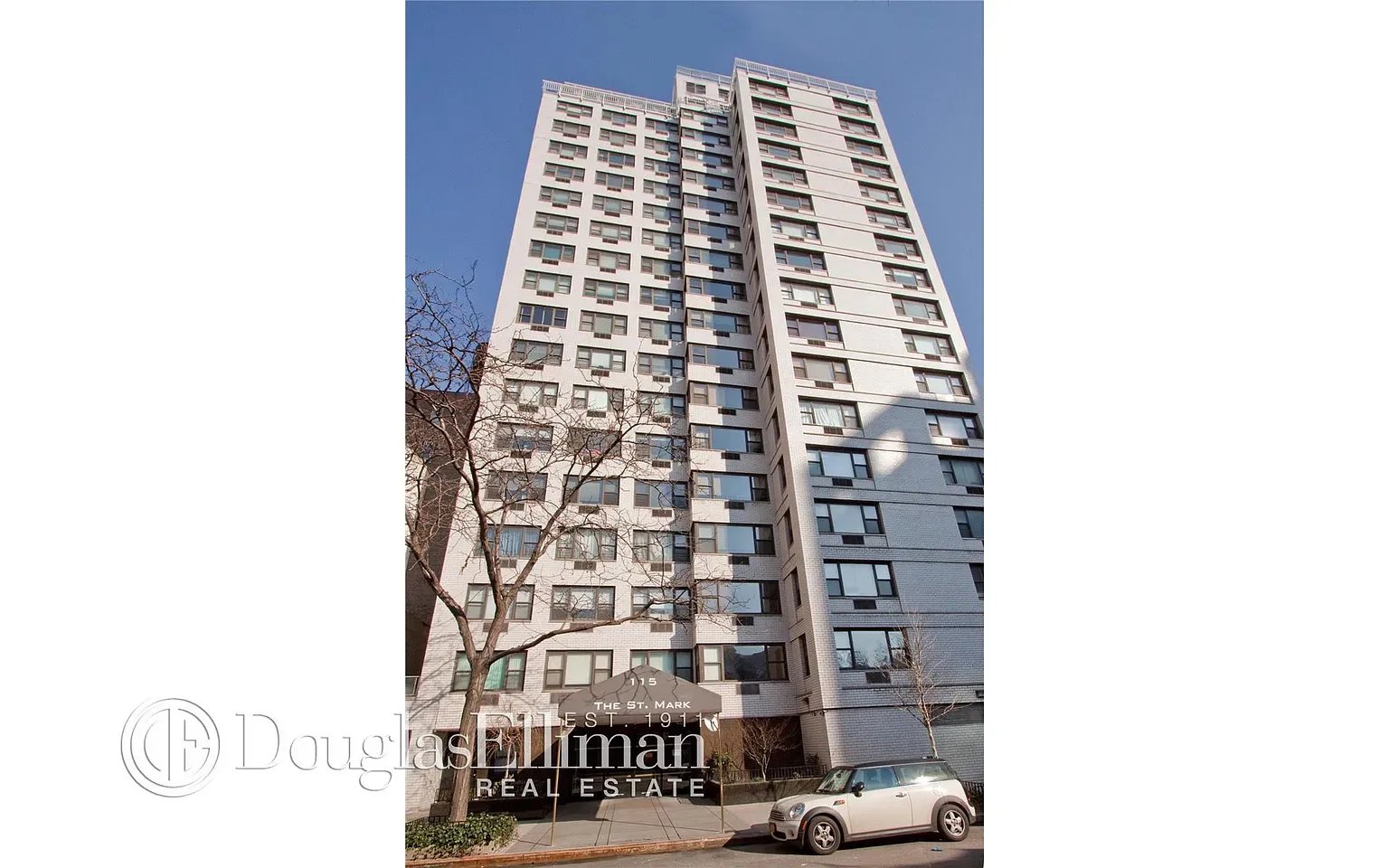 White high-rise apartment building with a street-level entrance canopy and bare trees.