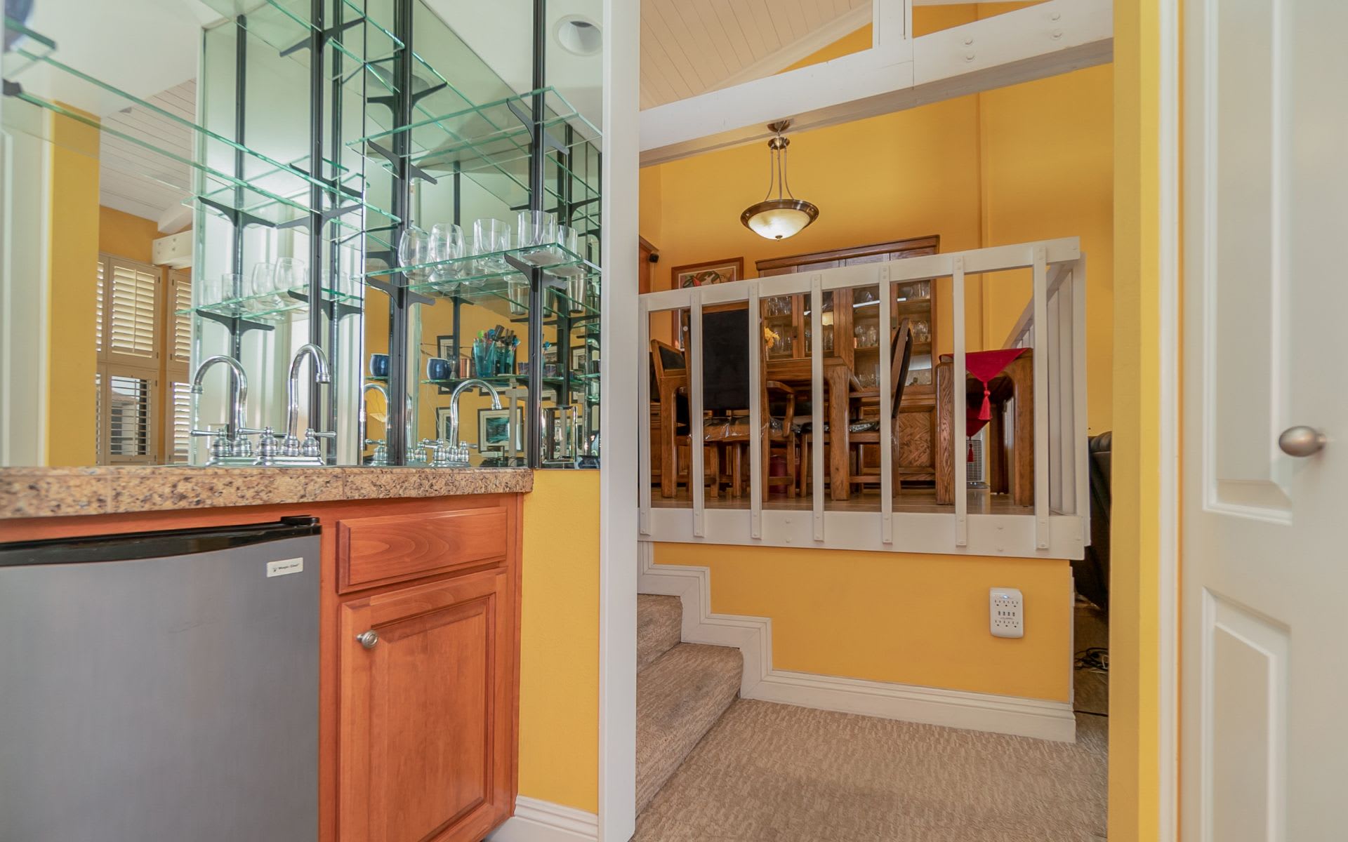 Wet bar with mirrored glass shelves and a granite counter beside stairs to the dining area.
