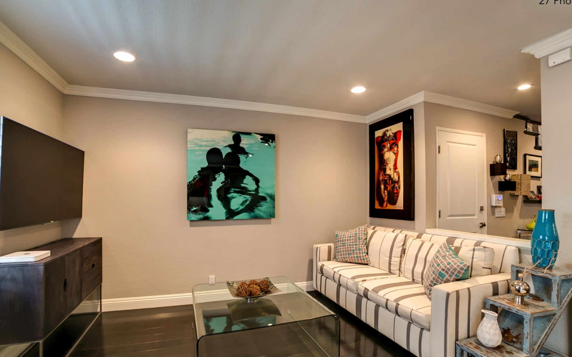 Living room with a white striped sofa, colorful wall art, and a wall-mounted television.