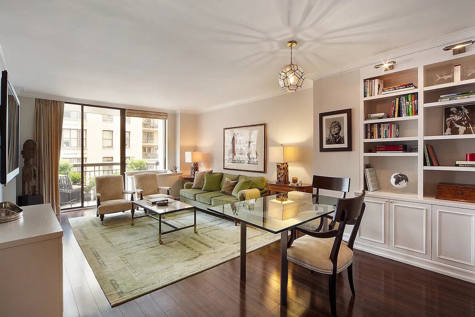 Furnished living and dining room with a green sofa, built-in bookshelves, and terrace doors.