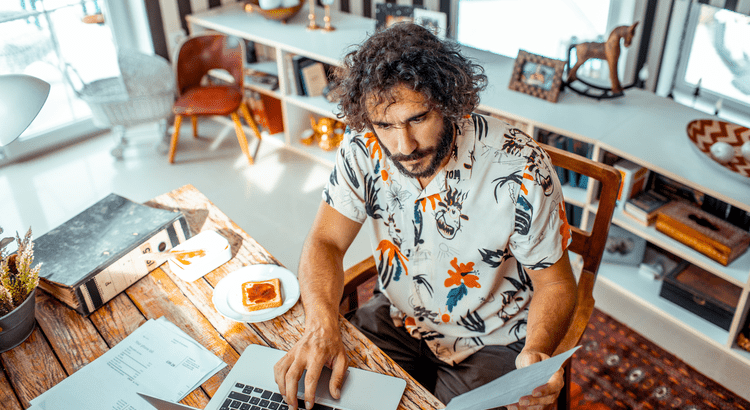 Person in brightly colored shirt on laptop with paperwork nearby