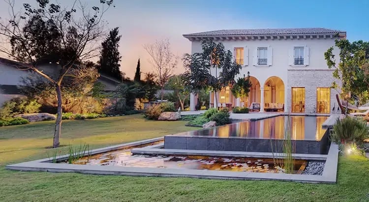 A luxurious house with a well-maintained garden and a pool in the foreground, captured at dusk. The scene exudes elegance and comfort.