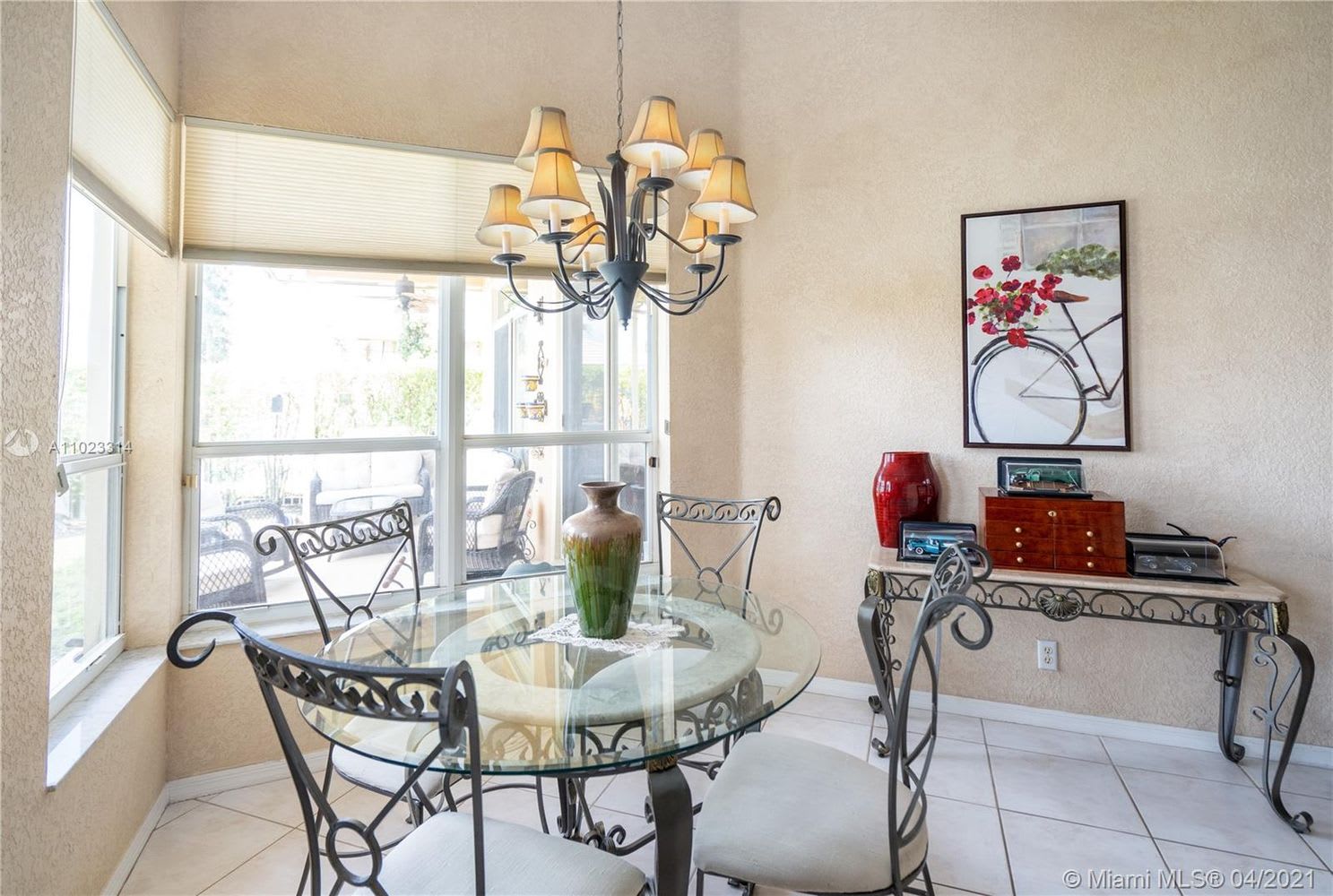 Dining room with a round glass table, ornate metal chairs, and large windows overlooking a patio.