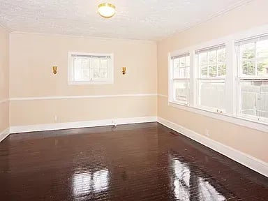 Empty room with peach walls, dark glossy hardwood floors, and large white-trimmed windows.