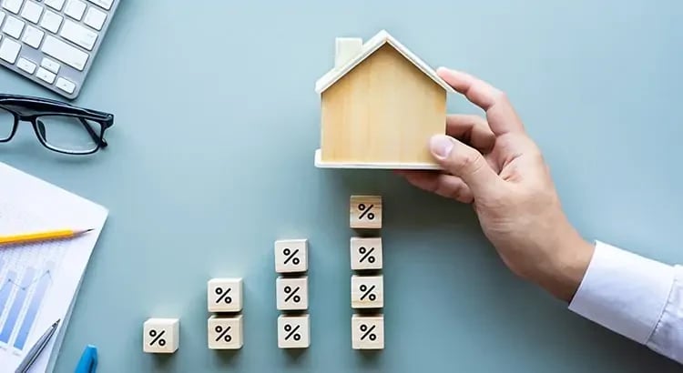 A person holding a small wooden house model above wooden blocks with symbols on them, likely representing planning or real estate concepts.