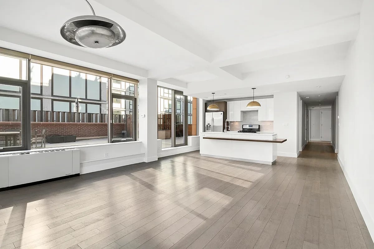 Open-plan living room and kitchen with a white island, wood floors, and large terrace-facing windows.