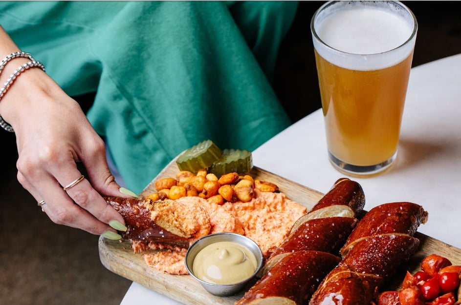 Oktoberfest platter of sausages, cheese spread, pickles, and mustard beside a foamy beer.