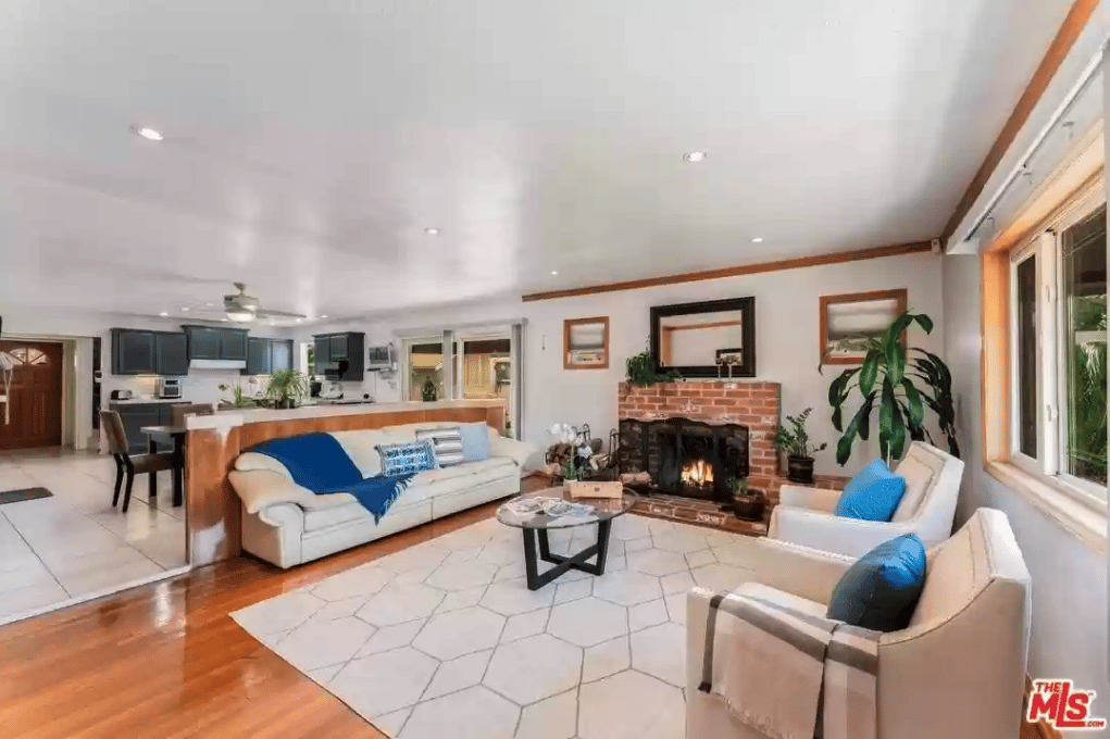 Open-plan living room with a brick fireplace, white seating, and large windows.