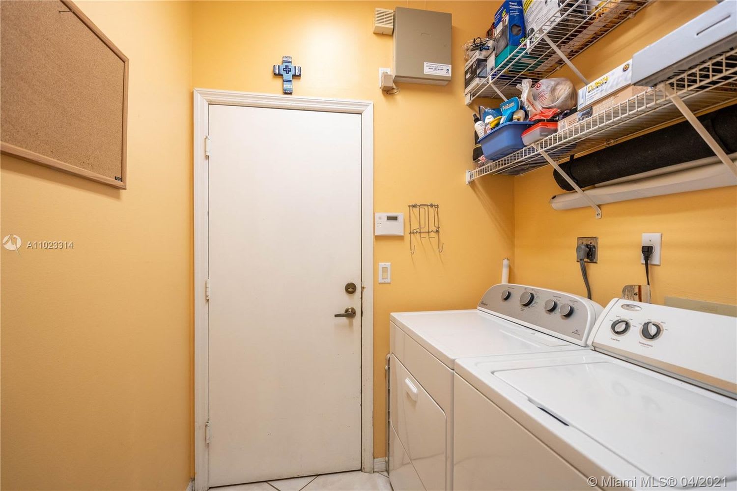 Laundry room with white washer and dryer beneath wire shelves stocked with household supplies.